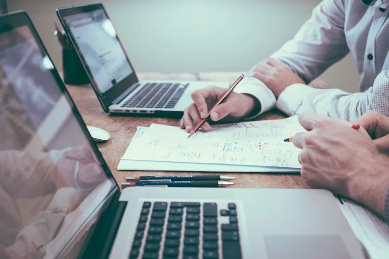 Two people at a desk going through paperwork and laptops together